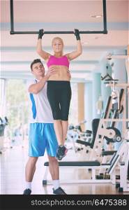 trainer support young woman while lifting on bar in fitness gym indoors. trainer support young woman while lifting on bar in fitness gym