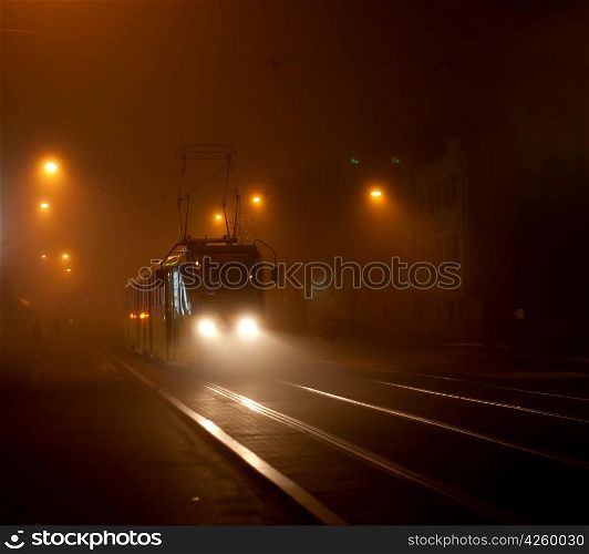 Tram moving on city street in the fog at night