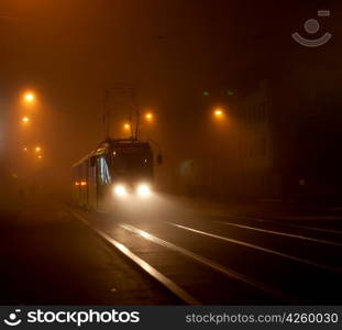 Tram moving on city street in the fog at night