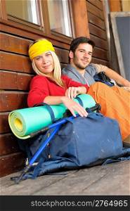 Tramping young couple backpack relax sitting by wooden cottage