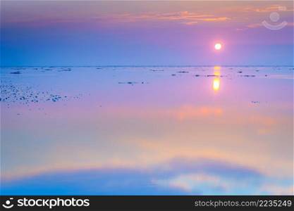 Tranquil and tranquil zen-like sunset on the beach with beautiful colors in pink and red with reflections on the water - Wadden Sea, Netherlands. Reflecting mudflats all twilight with setting sun