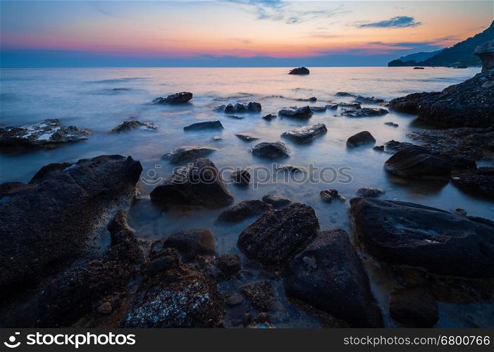 Tranquil coastal sunset on rocky beach; low shutter speed