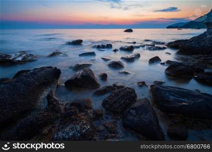 Tranquil coastal sunset on rocky beach; low shutter speed