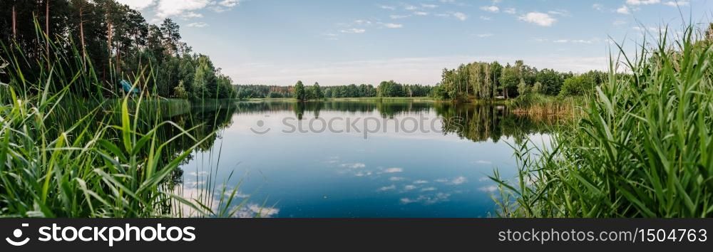 Tranquil landscape at a lake, with the vibrant blue sky, white clouds and the trees reflected symmetrically in the clean blue water. Summer. Lake with spring trees panorama photo.