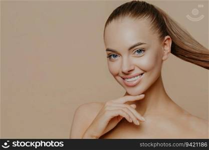 Tranquil woman, perfect skin, ponytail. Facial treatments, well cared complexion. Beige wall, empty space. Skin care concept.