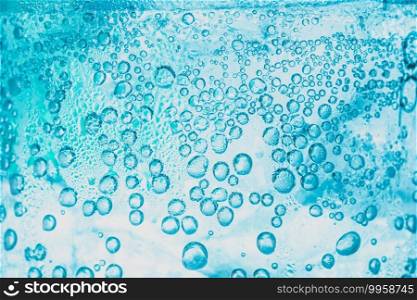 transparent background of soda water and ice with bright blue bubbles within the glass is abstract.