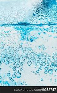 transparent background of soda water and ice with bright blue bubbles within the glass is abstract.