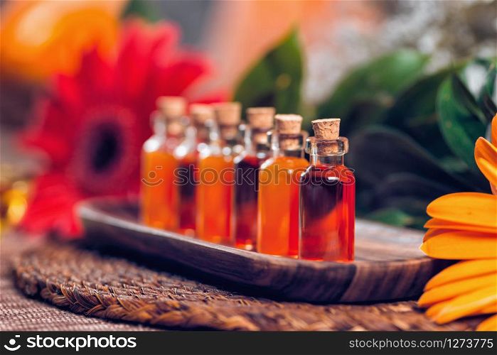 Transparent bottles filled with red and orange essential oils on wooden board. Red flower and Himalaya salt lamp background. Aromatherapy relax concept