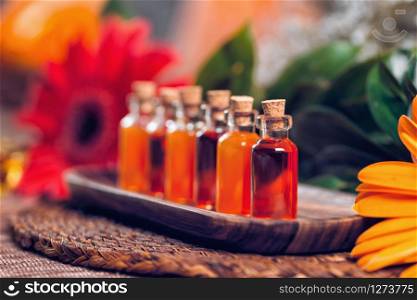 Transparent bottles filled with red and orange essential oils on wooden board. Red flower and Himalaya salt lamp background. Aromatherapy relax concept