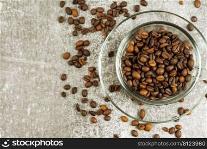 Transparent cup of coffee with coffee beans on gray concrete background with scattering of coffee beans. Arabica, Robusta. Drink for office, home. Top view, flat lay, mockup with copy space for text. Transparent coffee cup with roasted coffee beans on gray concrete backgfound with copy space.