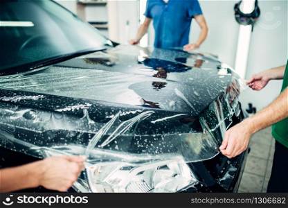 Transparent film, car paint protection installation process. Protect against chips and scratches. Workers wraps hood in protective coating