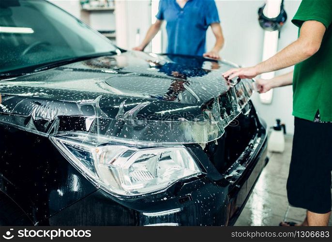 Transparent film, car paint protection installation process. Protect against chips and scratches. Workers wraps hood in protective coating. Transparent film, car paint protection