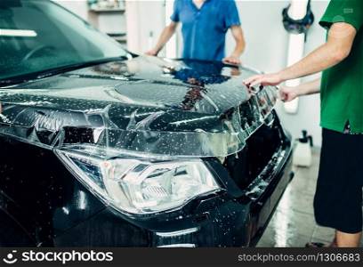 Transparent film, car paint protection installation process. Protect against chips and scratches. Workers wraps hood in protective coating. Transparent film, car paint protection