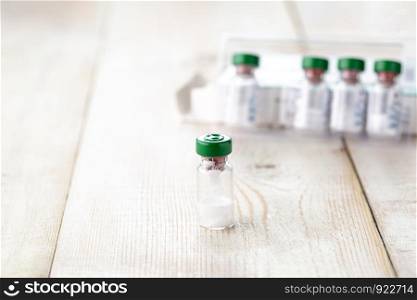 Transparent glass bottle of injectable medicine. Close-up, light wooden background. Transparent glass bottle of injectable medicine.