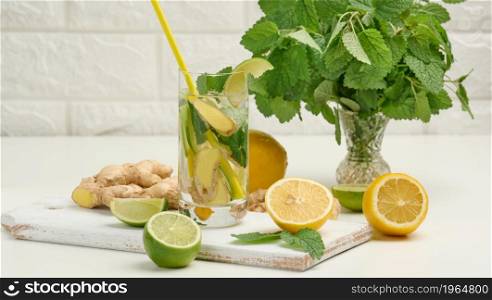 transparent glass cup with lemon, lime pieces and mint leaves and ginger pieces on a white table, detox.