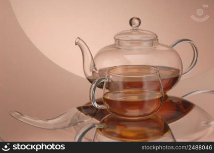 Transparent glass teapot and cup of tea on the reflective surface. Transparent glass teapot and cup with tea