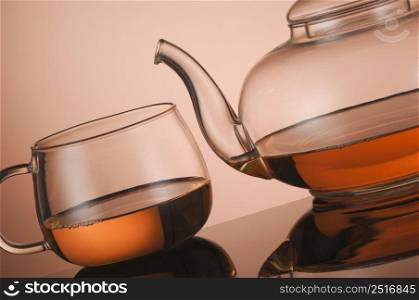 Transparent glass teapot and cup of tea on the reflective surface. Transparent glass teapot and cup with tea