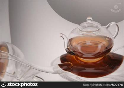 Transparent glass teapot with tea on the reflective surface on a light gray background. Transparent glass teapot and cup with tea