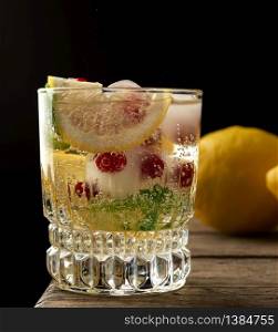 transparent glass with lemonade and pieces of ice, red berries, a refreshing summer drink on a black background