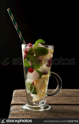 transparent glass with lemonade and pieces of ice, red berries and paper tubes, a refreshing summer drink on a black background