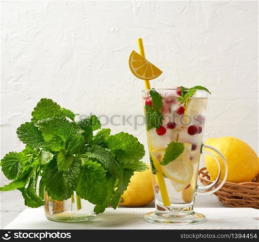 transparent glass with lemonade and pieces of ice, red berries and paper tubes, a refreshing summer drink