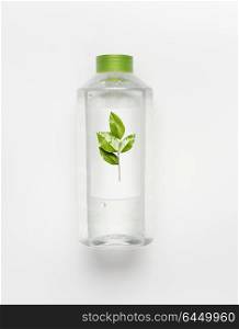Transparent liquid bottle with green lid. Clean nature water with green leaves and branding mock up on white desk background , top view.