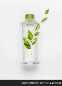 Transparent liquid bottle with green lid. Clear nature water with green flying leaves and branding mock up on white desk background , top view.