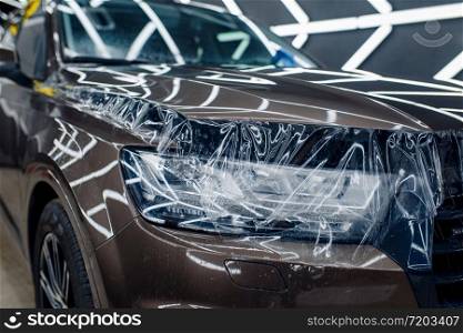 Transparent protection film on car hood, nobody. Installation of coating that protects the paint of automobile from scratches. New vehicle in garage, tuning procedure. Transparent protection film on car hood, nobody