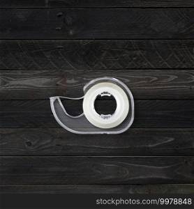 Transparent scotch tape dispenser isolated on black wood background. Scotch tape dispenser isolated on black wood background