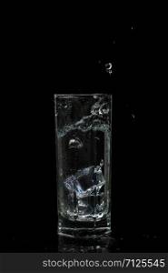 transparent water glass with ice cubes on black isolated glass background