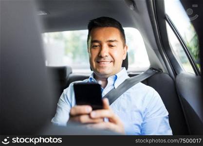 transport, business and communication concept - smiling male passenger or businessman using smartphone on back seat of taxi car. passenger or businessman using smartphone in car