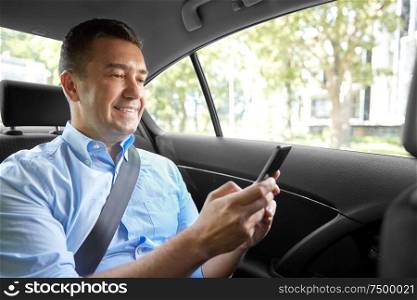 transport, business and communication concept - smiling male passenger or businessman using smartphone on back seat of taxi car. passenger or businessman using smartphone in car