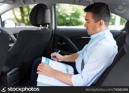 transport, business and corporate concept - businessman with charts in folder working on back seat of taxi car. businessman with coffee on car back seat