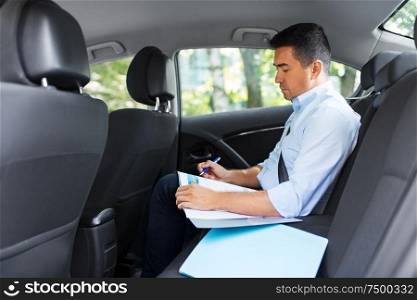 transport, business and corporate concept - businessman with charts in folder working on back seat of taxi car. businessman with coffee on car back seat