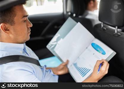 transport, business and corporate concept - businessman with charts in folder working on back seat of taxi car. businessman with coffee on car back seat