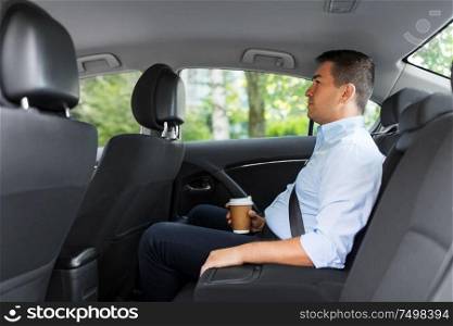transport, business and people concept - businessman drinking takeaway coffee on back seat of taxi car. businessman with takeaway coffee on car back seat