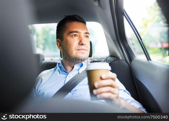 transport, business and people concept - businessman drinking takeaway coffee on back seat of taxi car. businessman with takeaway coffee on car back seat