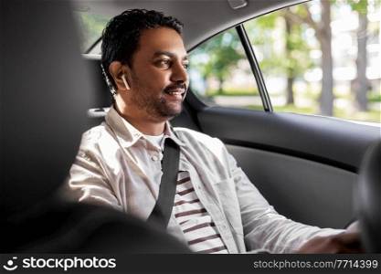transport, business and technology concept - happy smiling indian male passenger with wireless earphones on back seat of taxi car. indian male passenger with earphones in taxi car