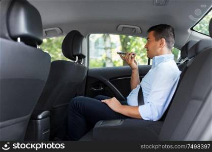 transport, business and technology concept - male passenger or businessman using voice command recorder on smartphone on back seat of taxi car. male passenger calling on smartphone in taxi car