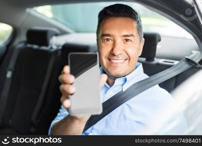 transport, business and technology concept - smiling male passenger or businessman showing smartphone on back seat of taxi car. passenger or businessman showing smartphone in car