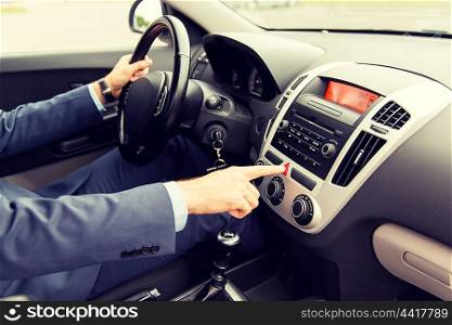 transport, business trip, breakdown, technology and people concept - close up of young man in suit driving car and switching emergency signal button