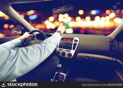 transport, business trip, direction and people concept - close up of young man driving car and pointing finger to something over city night lights background. close up of man driving car and pointing finger