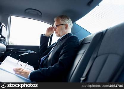 transport, business trip, paperwork and people concept - senior businessman with documents driving on car back seat