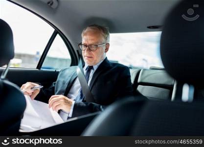 transport, business trip, paperwork and people concept - senior businessman with documents and pen driving on car back seat
