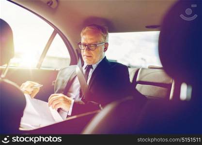 transport, business trip, paperwork and people concept - senior businessman with documents and pen driving on car back seat. senior businessman with papers driving in car
