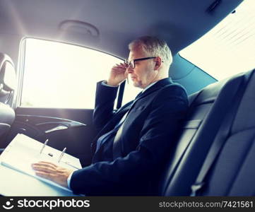 transport, business trip, paperwork and people concept - senior businessman with documents driving on car back seat. senior businessman with papers driving in car