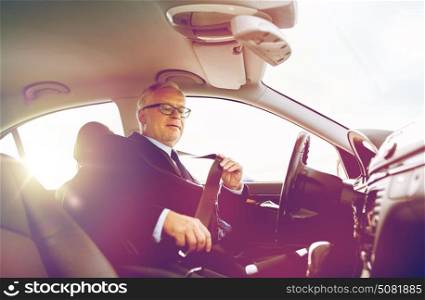 transport, business trip, safety and people concept - senior businessman fastening seat belt before driving car. senior businessman fastening car seat belt
