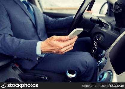 transport, business trip, technology and people concept - close up of businessman in suit with smartphone driving car