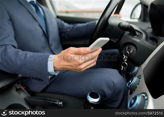 transport, business trip, technology and people concept - close up of businessman in suit with smartphone driving car