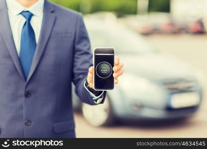 transport, business trip, technology and people concept - close up of man showing smartphone with ignition starter remote control application on screen on car parking